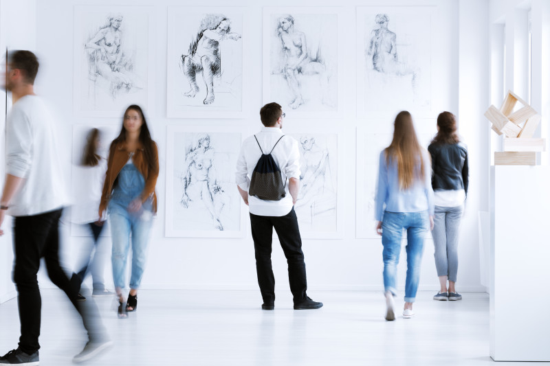 Young man with rucksack on back visiting art gallery with drawings and sculpture